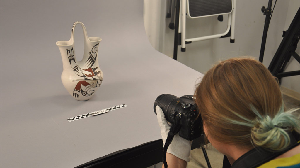 museum employee photographing a white vase with various red and black patterns