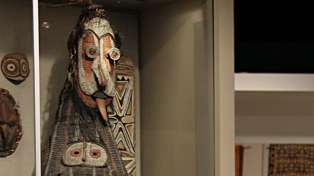 photo of tall oceanic dance mask with tongue sticking out in an exhibit case