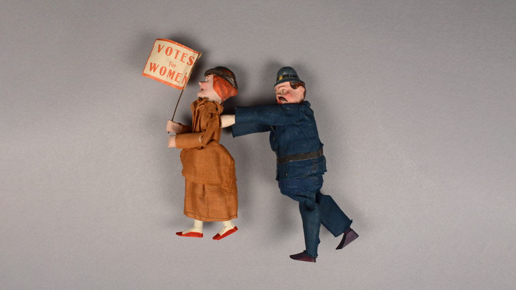 A figurine of a woman protesting Women Rights with a male cop figurine arresting her on a gray background