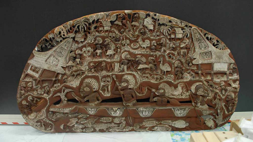 large, oval, wooden story board carved with scenes from everyday life