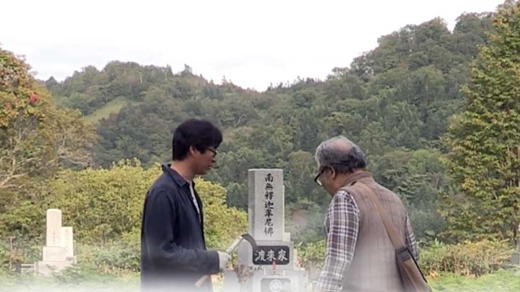 Two Korean men gather around a grave in a Korean cemetary