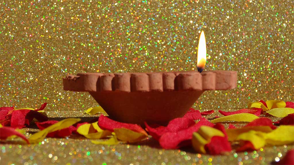 small terracotta burner with flame on a bed of petals against a gold backdrop