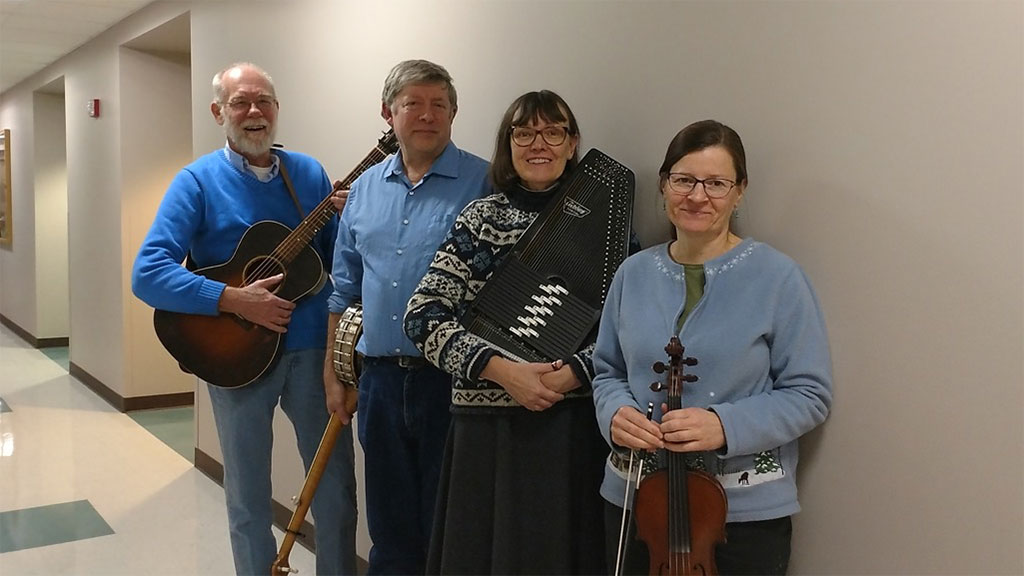 Quartet of 2 men and 2 women posing in a hallway with their old-time instruments