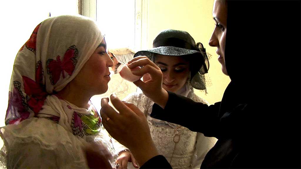 a woman applies makeup to an actress wearing a headscarf