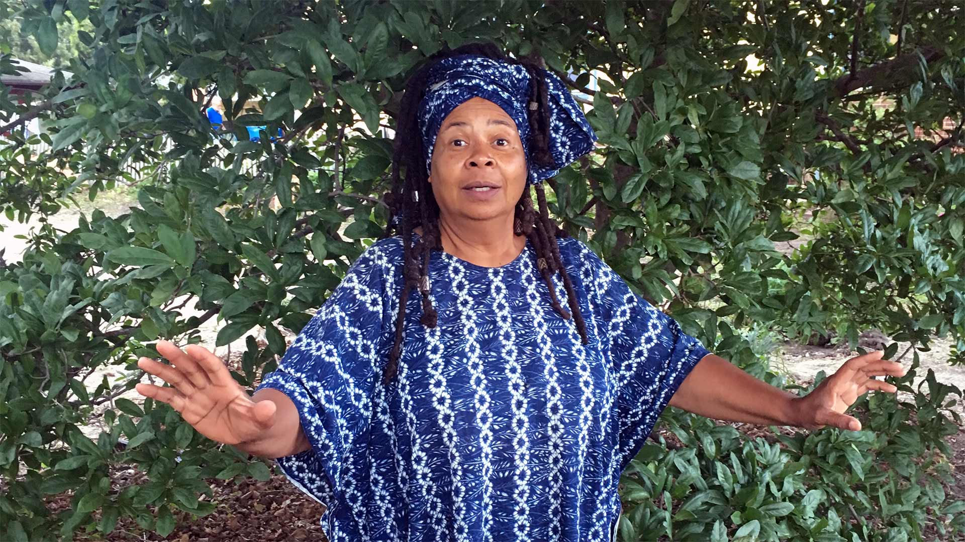 Dawn Blackman poses outdoors with arms outstretched in front of a large bush.