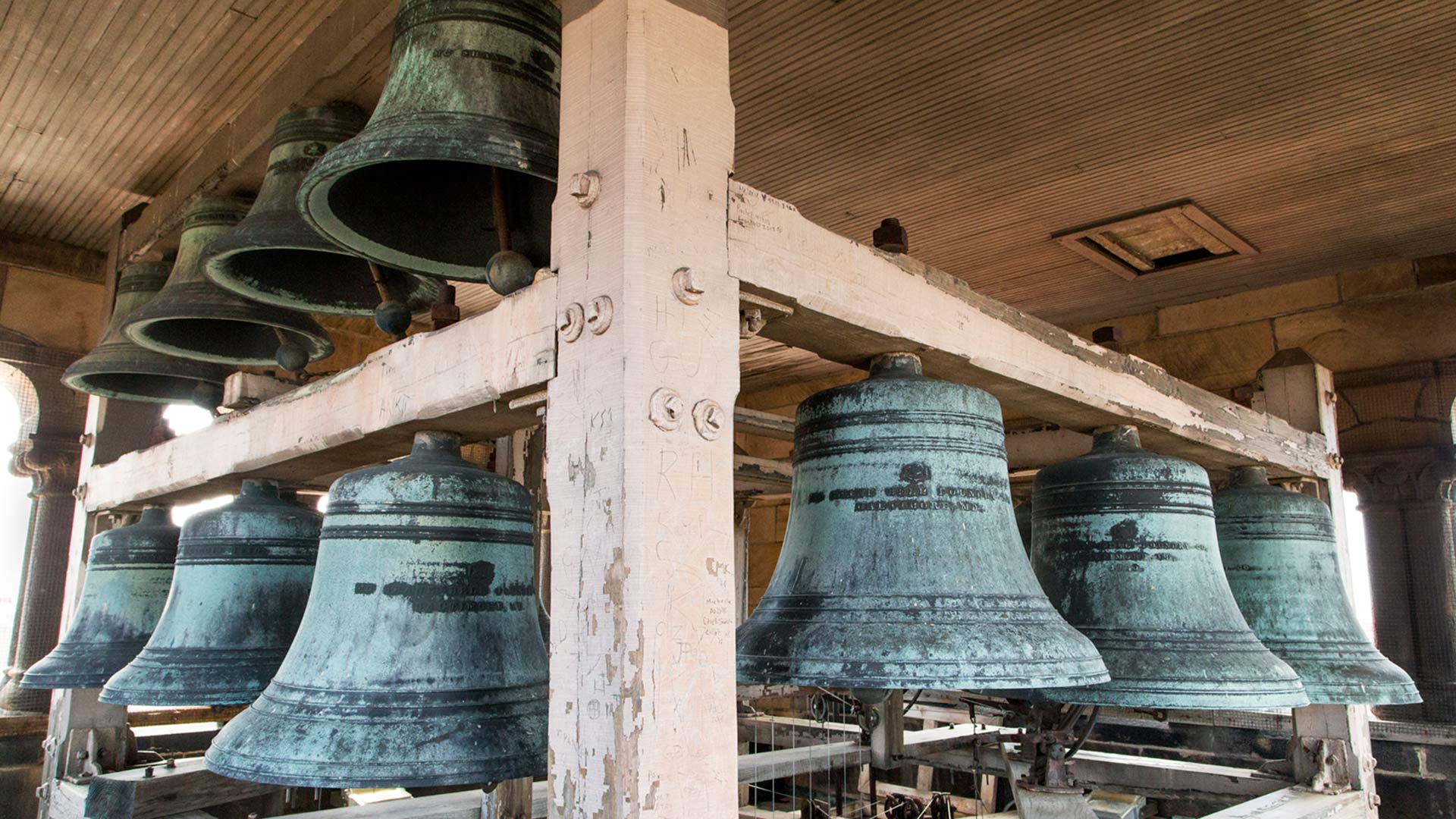 Large bells, textured bluish gray hanging from wooden beams