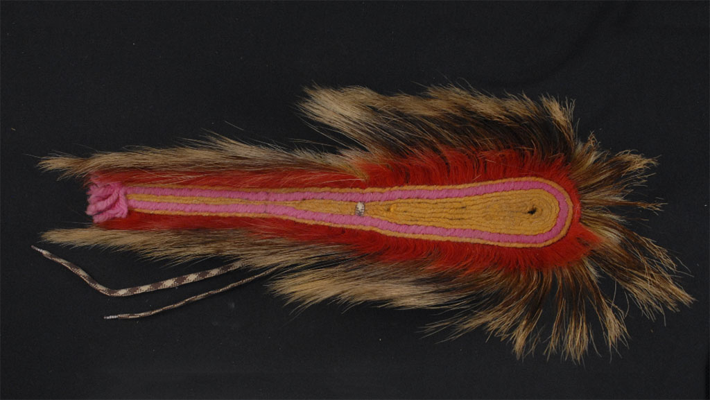 long object with a design of pink and yellow cord and red and tan fur or feathers