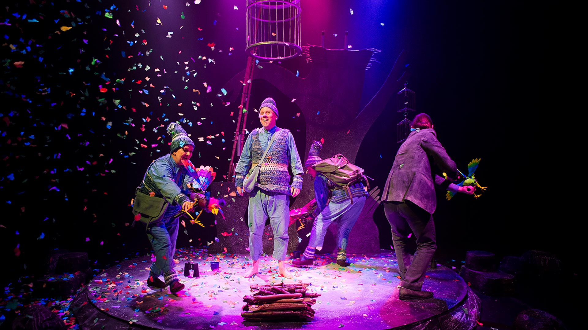 four people celebrating on stage, confetti in a purple-blue spotlight 