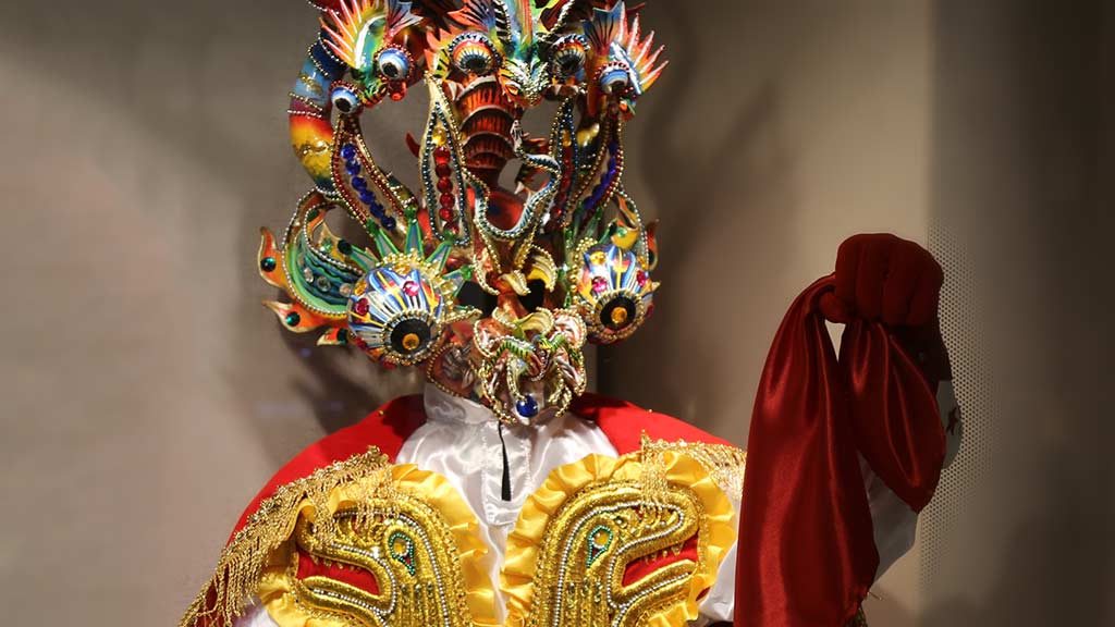 brightly colored festival costume with golden reptile design and many-eyed detailed devil mask