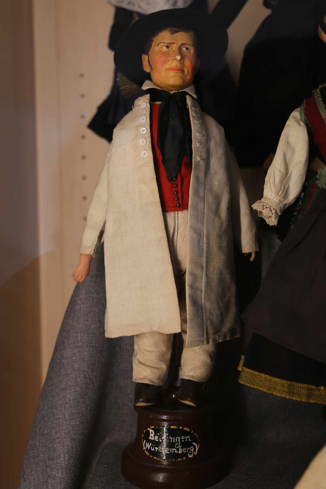 male doll wearing a hat, gray coat, and red vest
