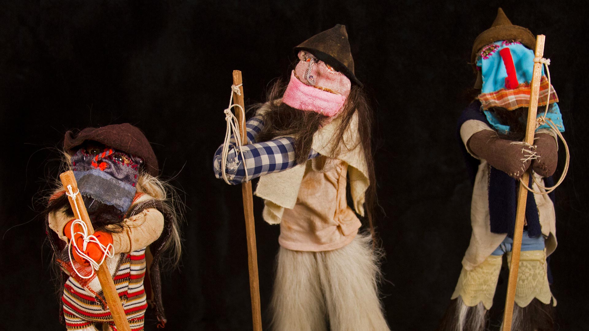 three faceless dolls made of mismatched fabrics, holding brooms