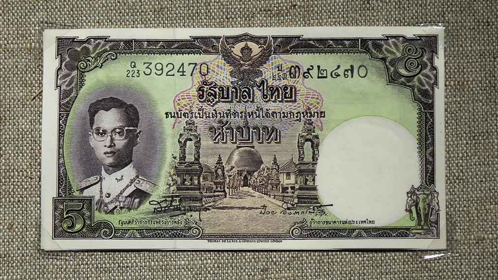 paper bank note showing Thai king and Buddhist temple