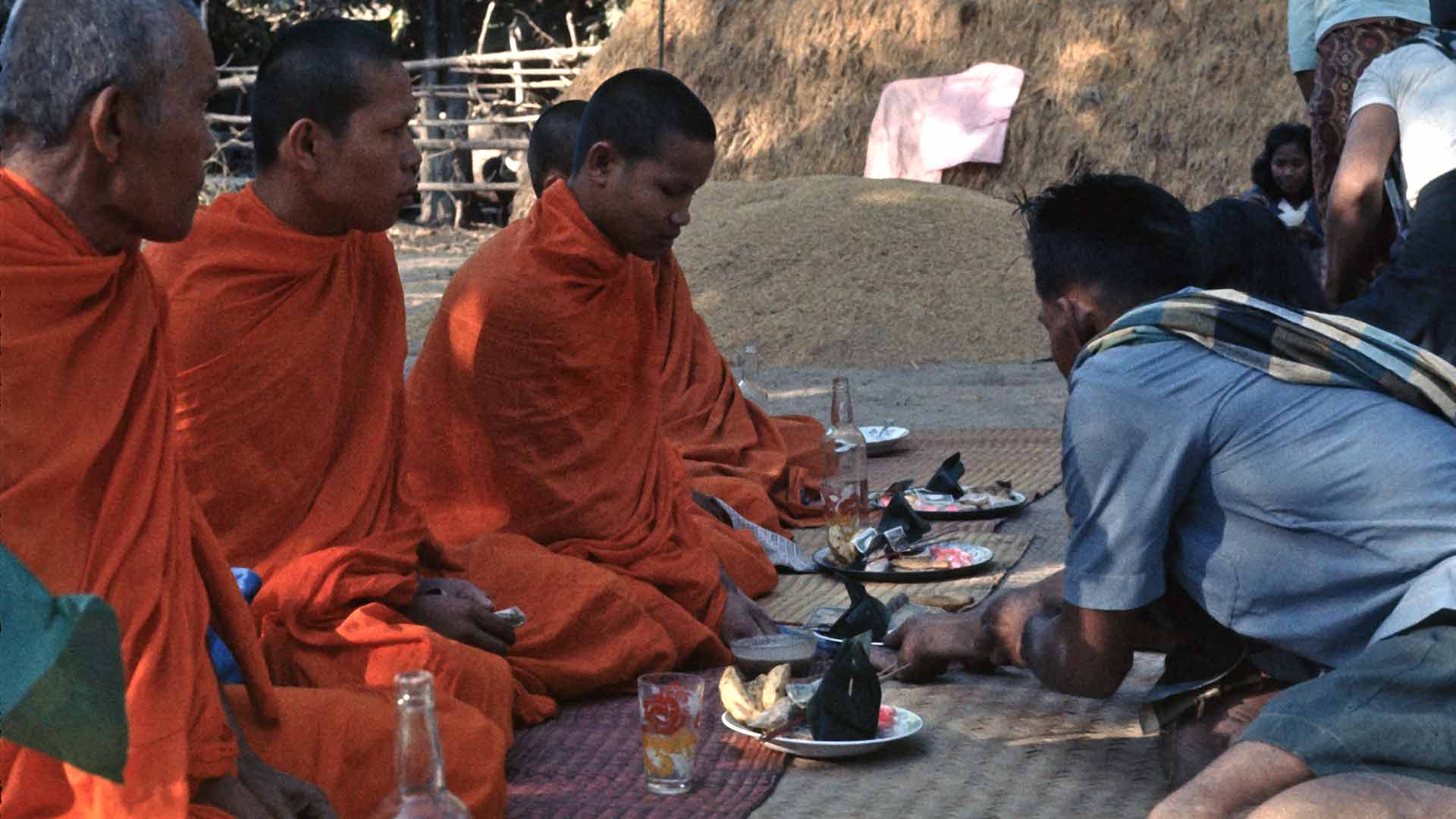 A man presents a dish of food to seated monks