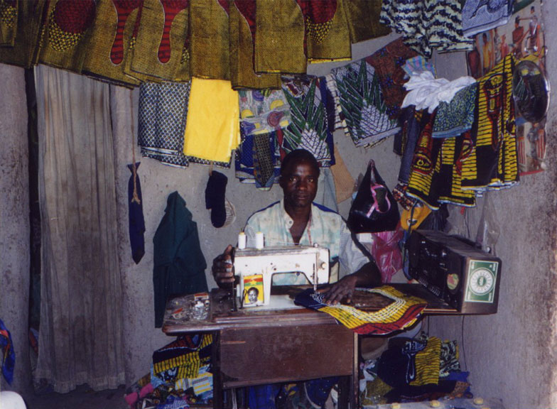 a tailor sitting at a sewing machine surrounded by vaious cloths