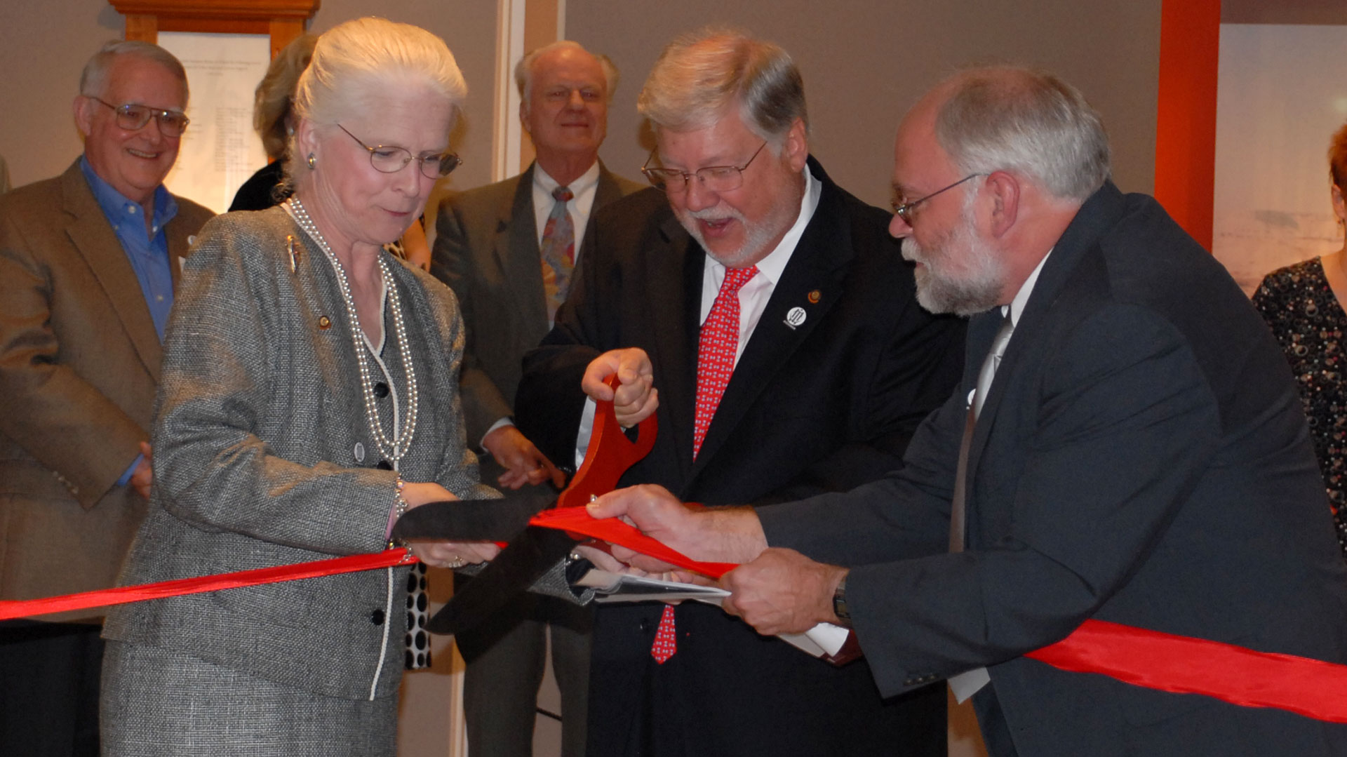 donors and Museum director cut red ribbon with large scissors