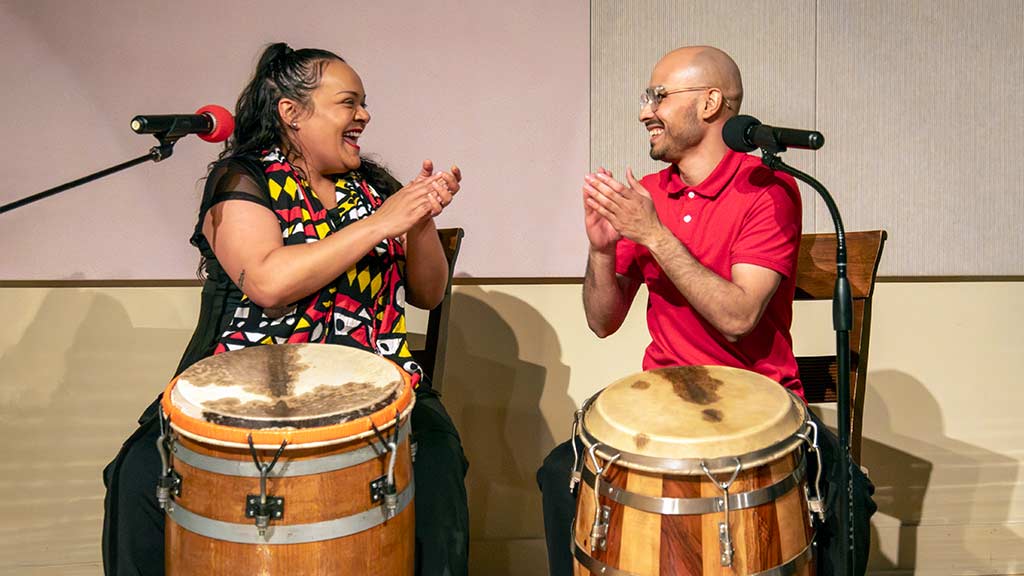 two drummers on stage clap and smile at each other