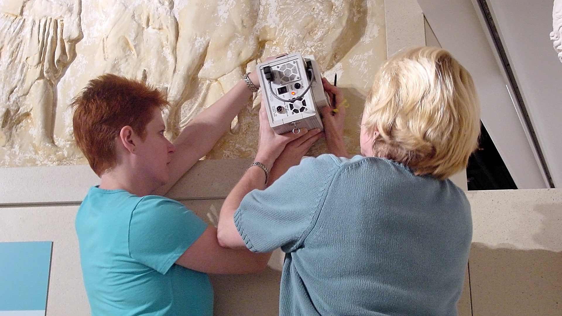 Two women hold a electronic box up to collect a measurement