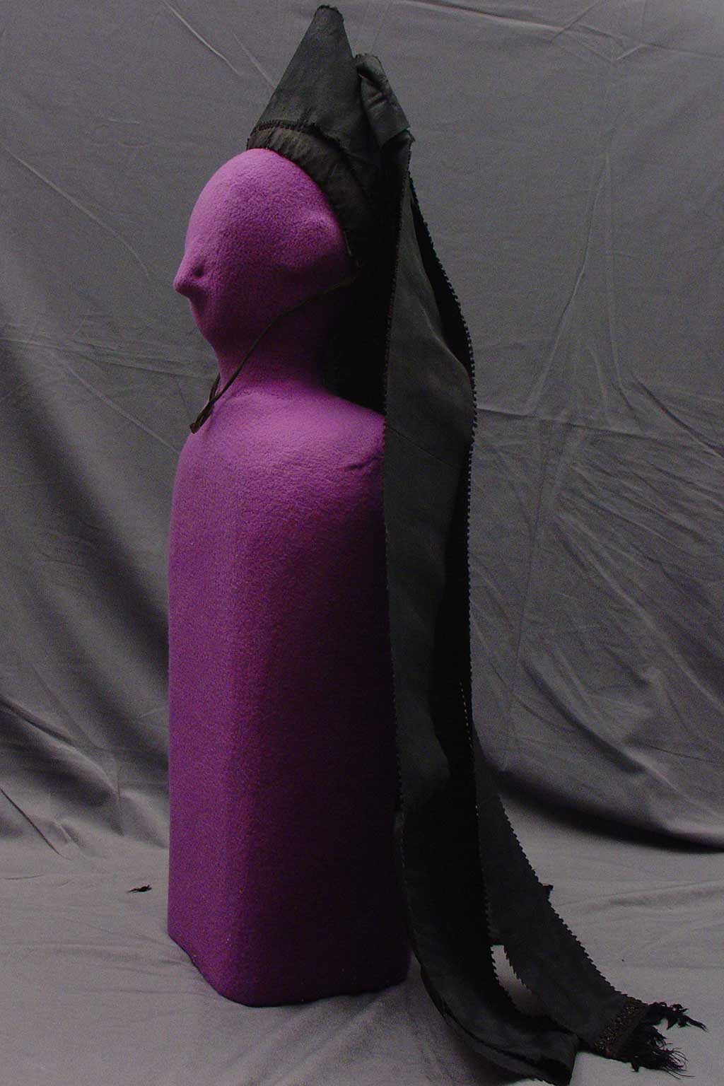 profile view, Conical bonnet covered in black silk, with two lengths of the same material doubled and extending down the back.