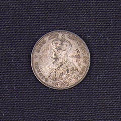 A worn silver tinted coin of a man's profile with a crown, text looping around the outer edge