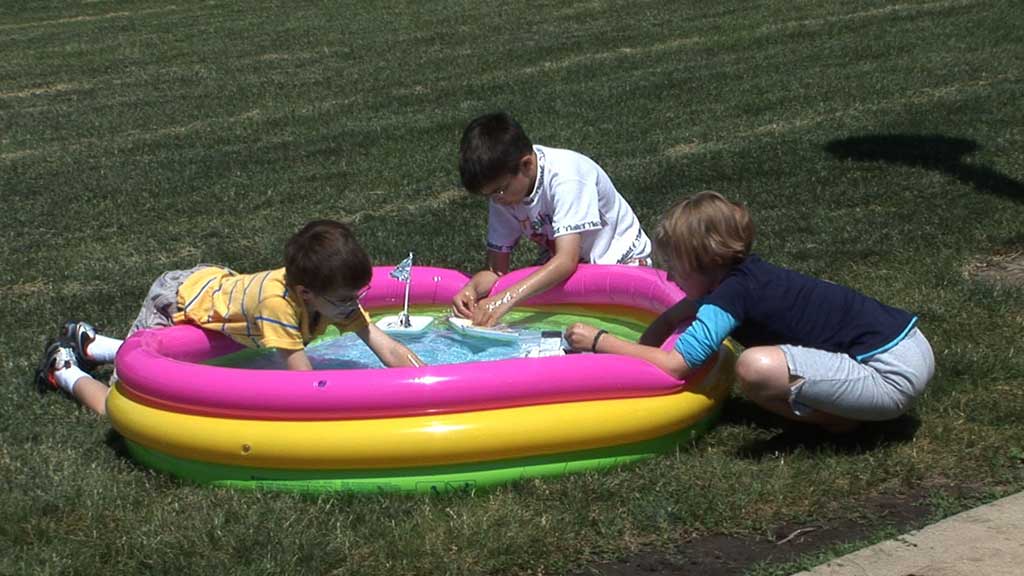 kids play with boats in a small inflatable pool
