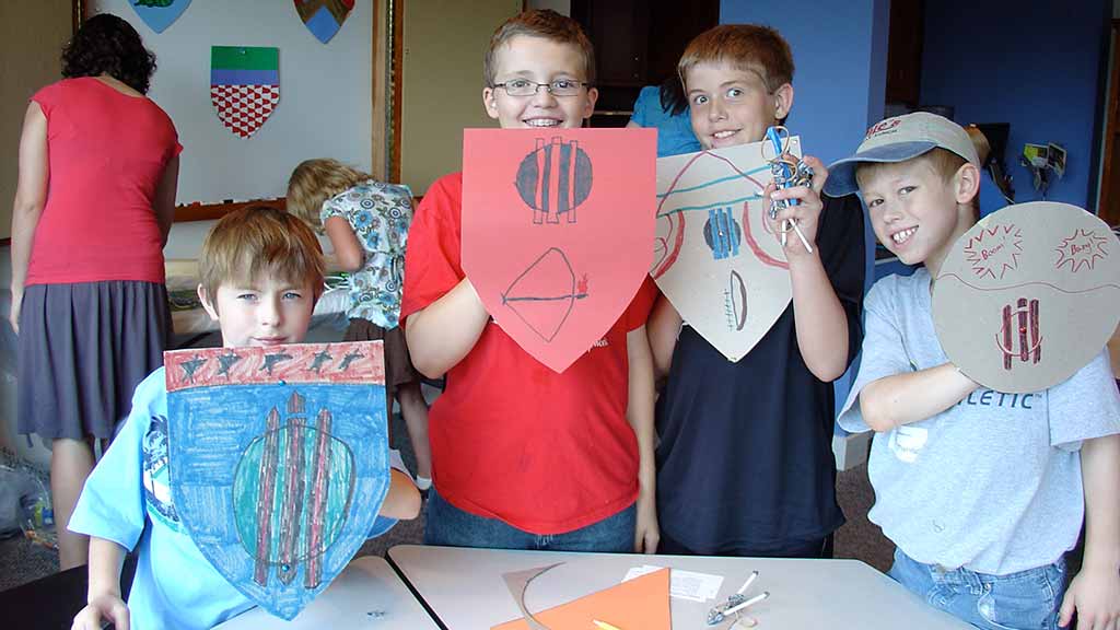 kids holding up their coat of arms they had colored on shields