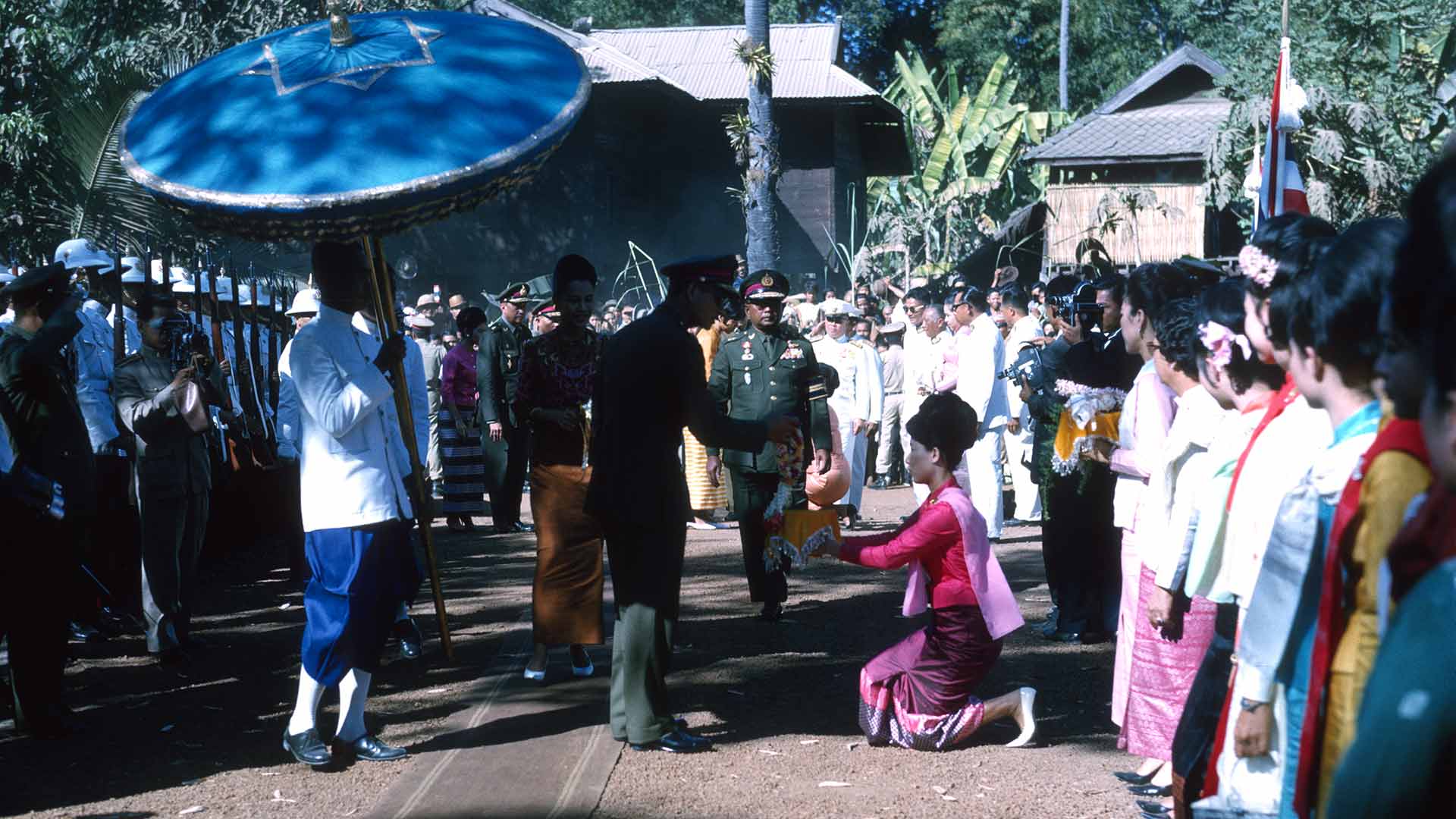 A young woman kneels to present a gift to a man in a military uniform.