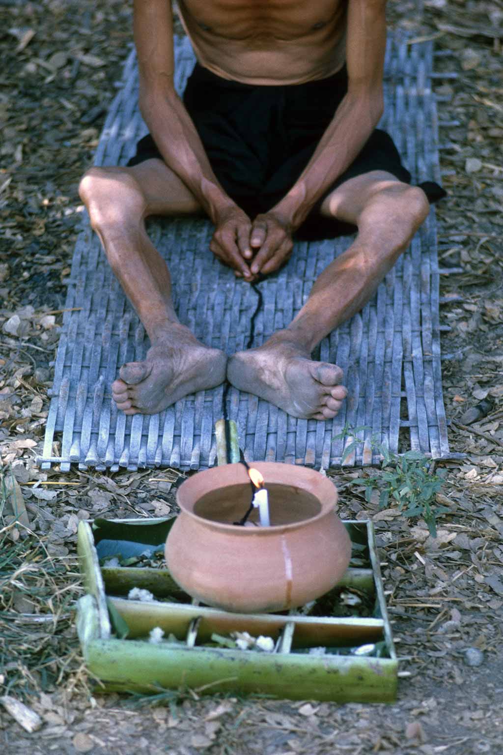 Closeup of black string held by man that ends inside a clay pot with a lit candle
