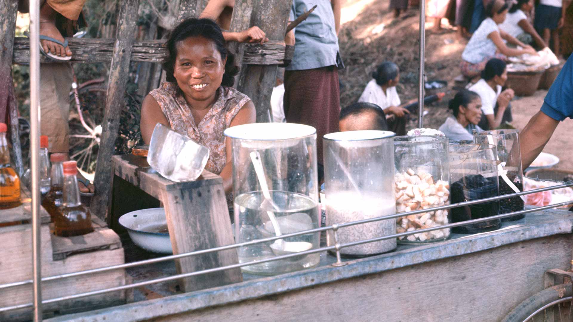 A girl sits behind good for sale at a food cart.