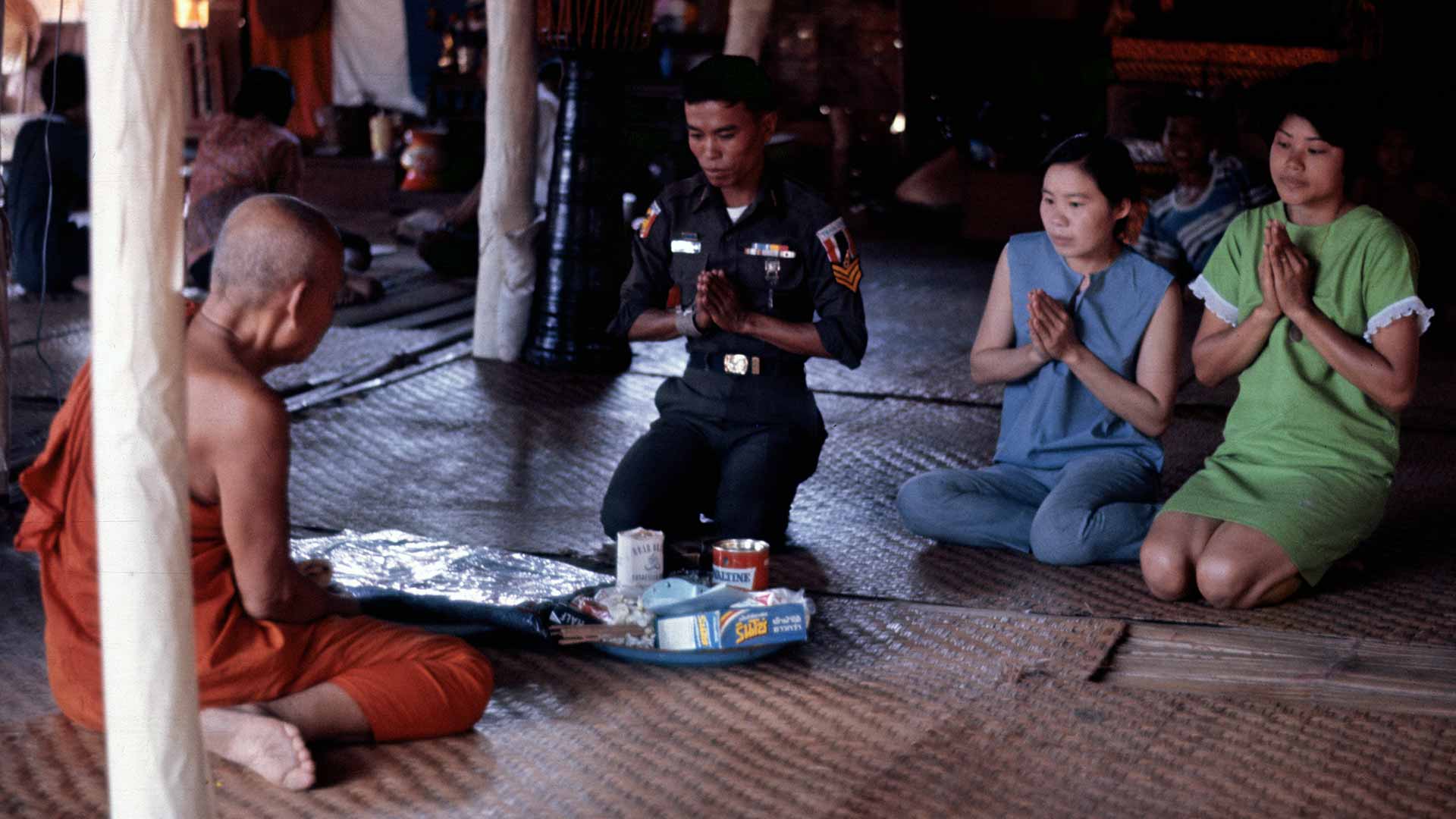 3 people pray and present offerings a seated monk