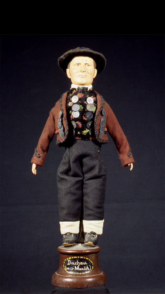 male doll wearing a brown jacket, black hat, and black pants