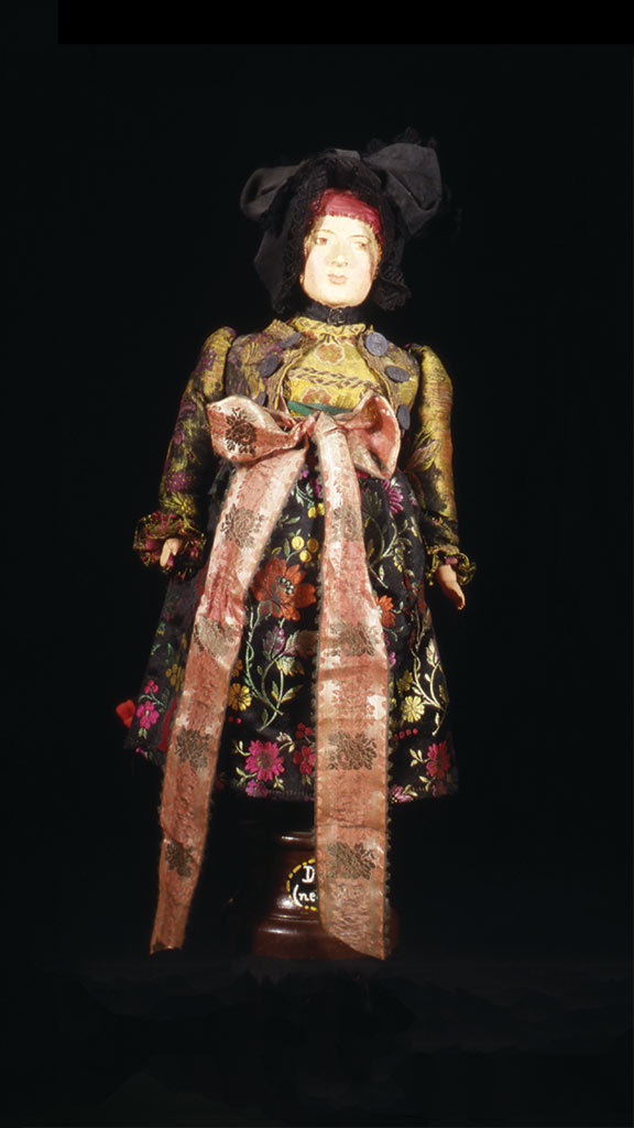 female doll wearing a gold and black dress with floral patterns and a bow