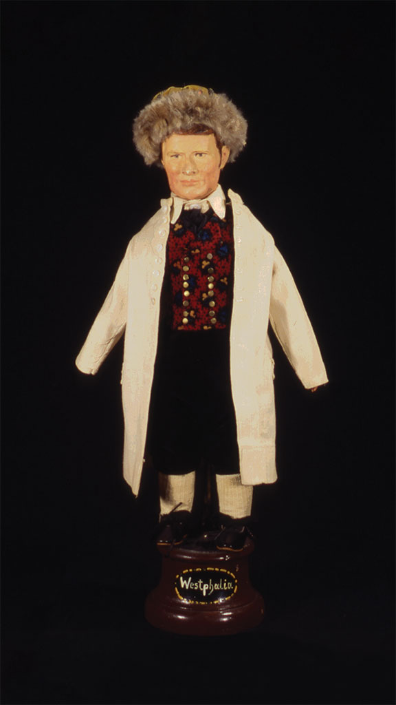 male doll with afro white hair wearing a white jacket, red shirt, and black pants