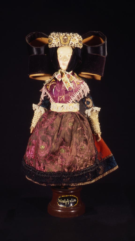 female doll wearing a brown and pink dress and an elaborate bow on the top of her head