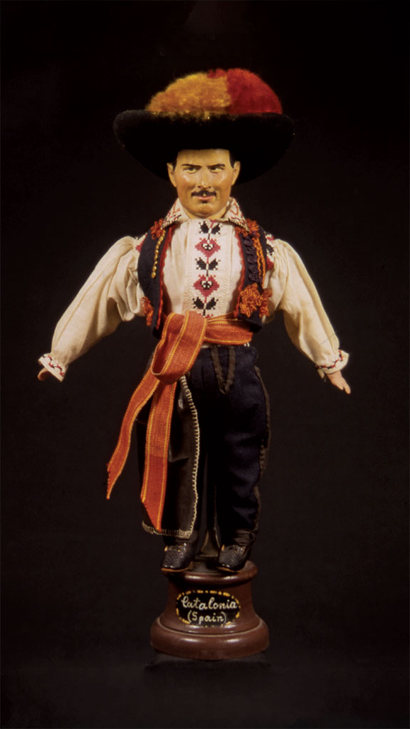male doll wearing a white shirt and black pants with an orange and red hat