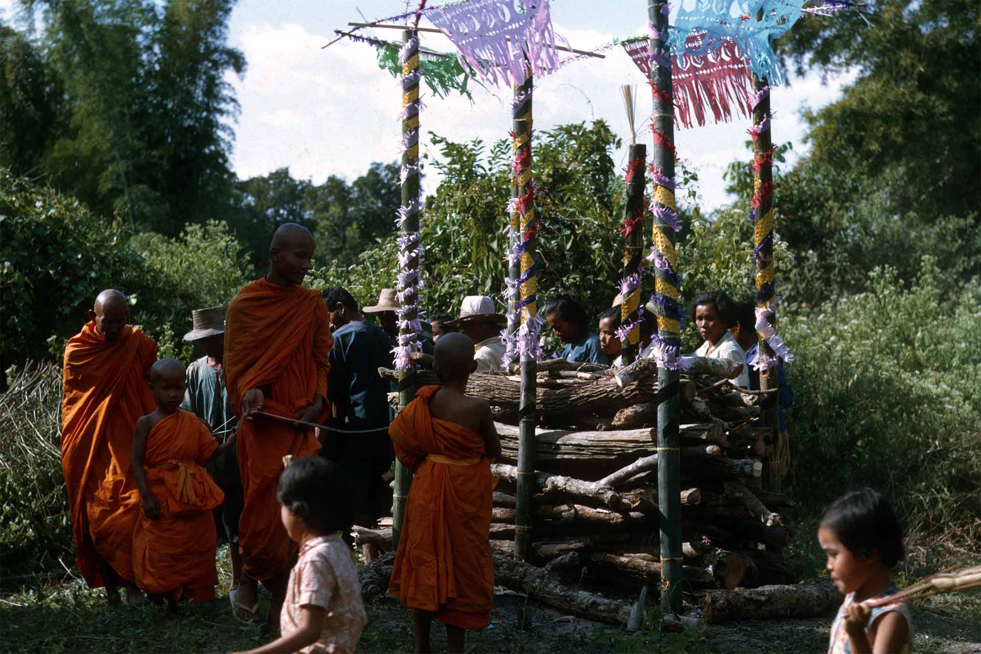 wood piled in funeral pyre, monks and villagers surrounding