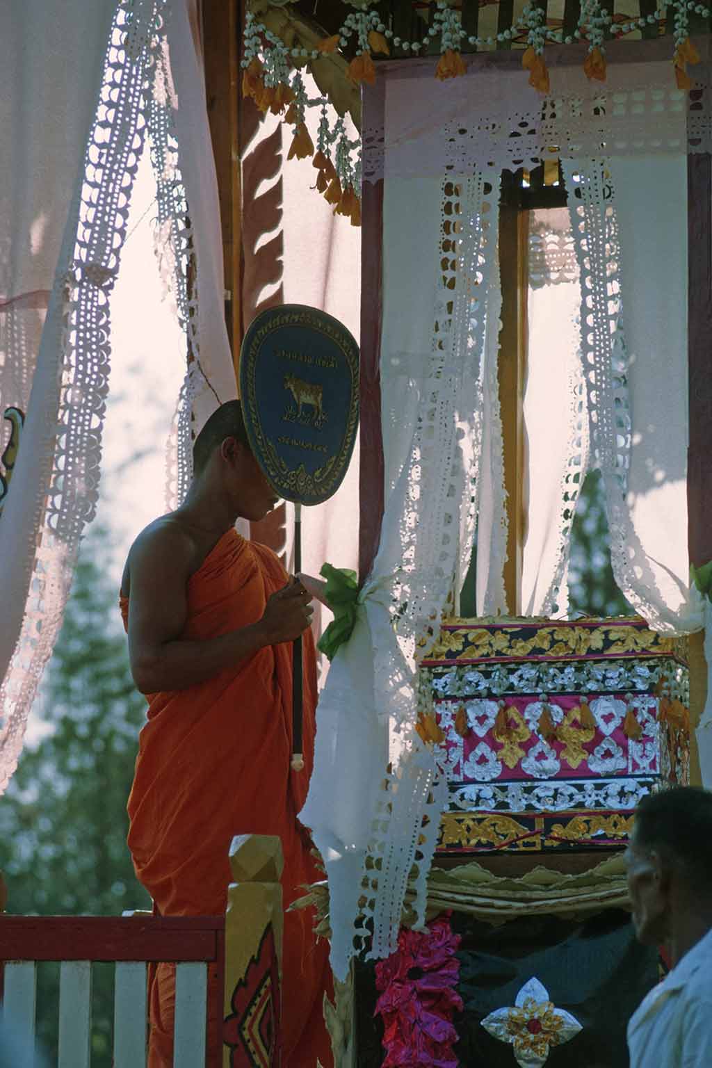 monk holding ceremonial fan adjacent to pyre