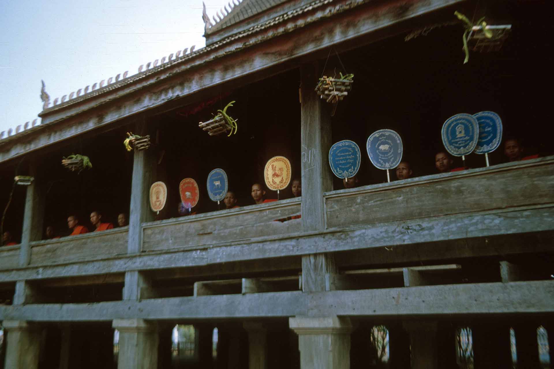 many monks holding ceremonial fan on balcony of building