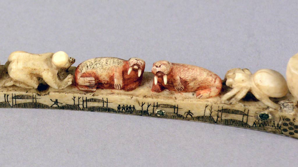 carvings of a human, two walruses, and a spider all lying atop an ivory pipe