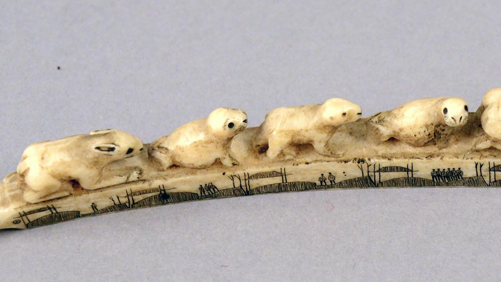 carvings of a rabbit and three seals lying atop an ivory pipe