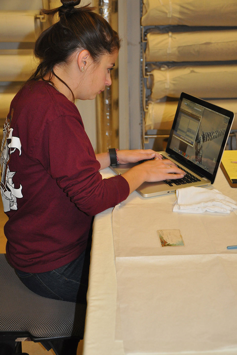 Tatiana, sitting in a chair, typing a report on a laptop about an artifact at the Spurlock Museum.