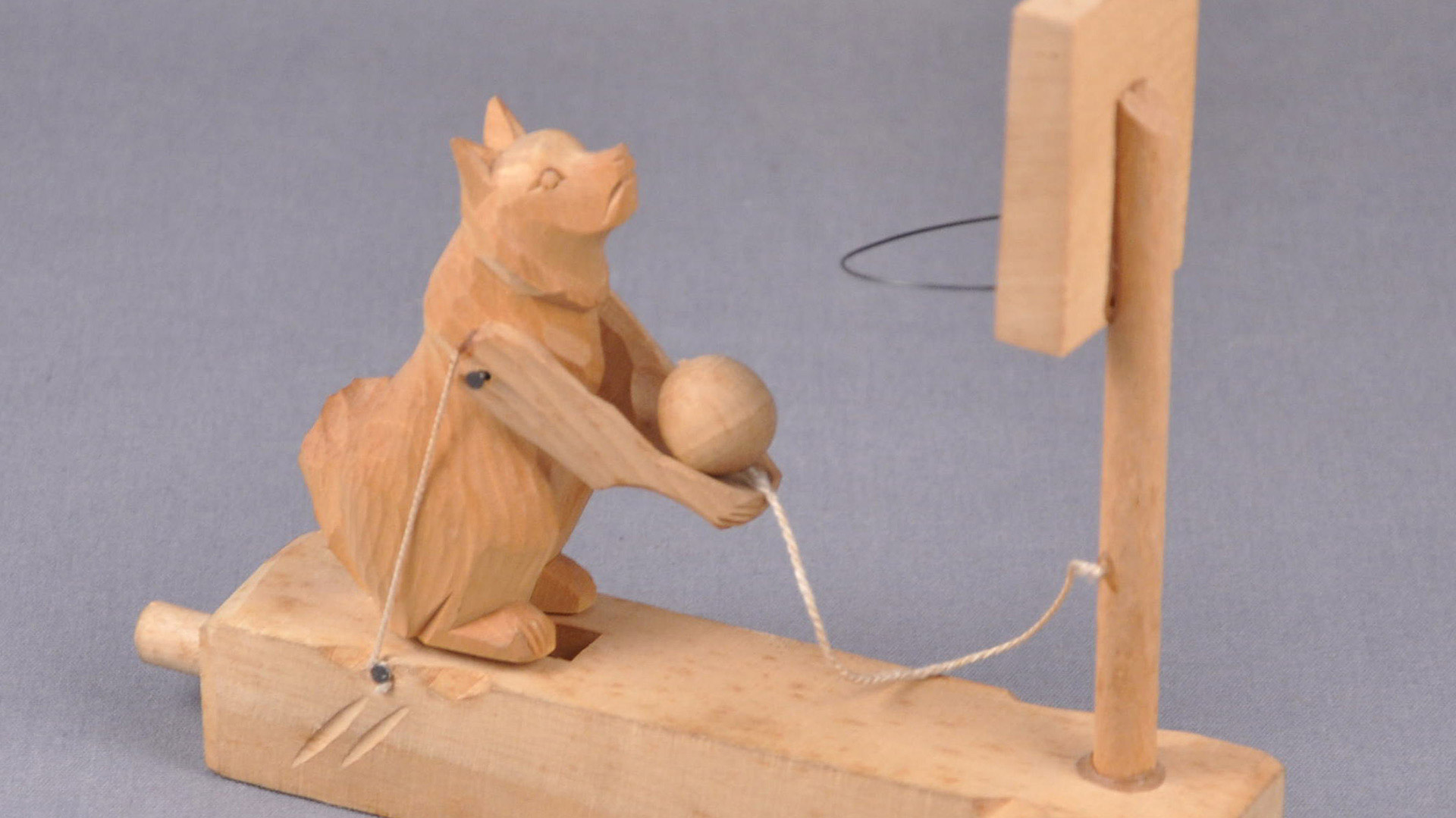Child's toy: a wood carving of a fox holding a sphere. A string attaches the wooden sphere to a wooden basketball hoop
