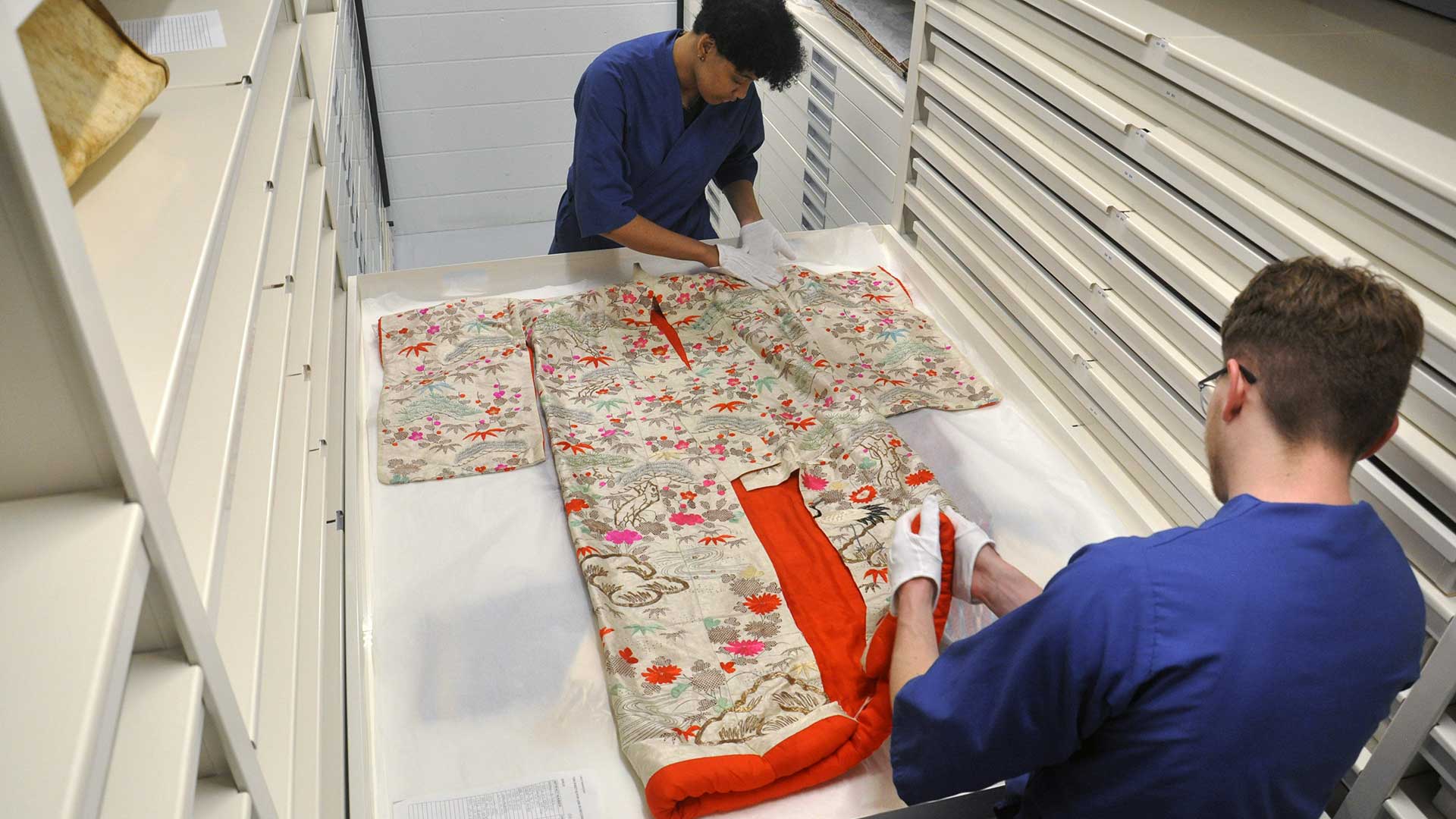 Kyndal and another student arrange a kimono in a storage drawer