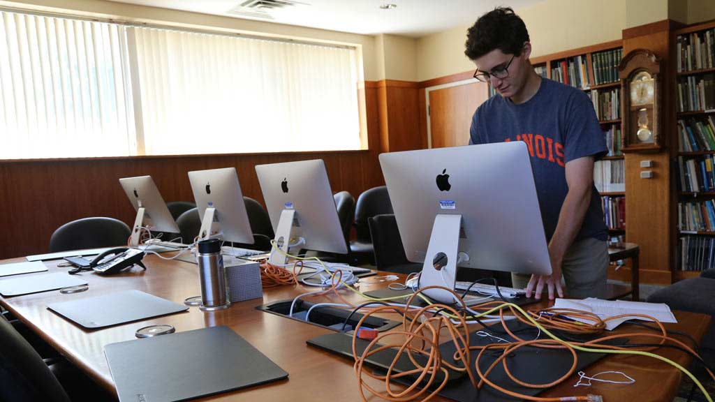 David in the conference room of the Spurlock Museum looking at one iMac with several iMacs next to him