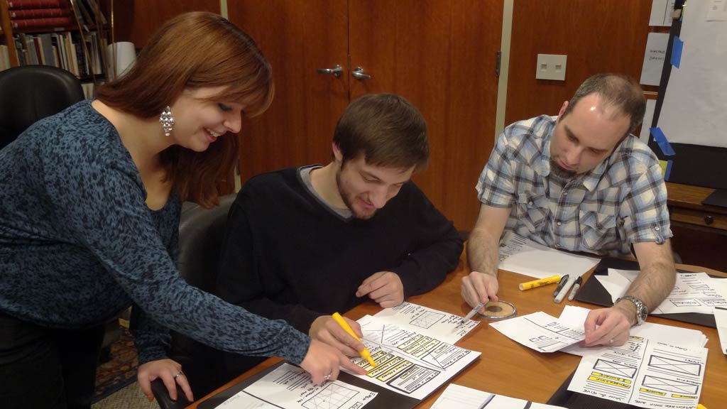  a woman and a man leaning towards Andy as they look at a piece of paper