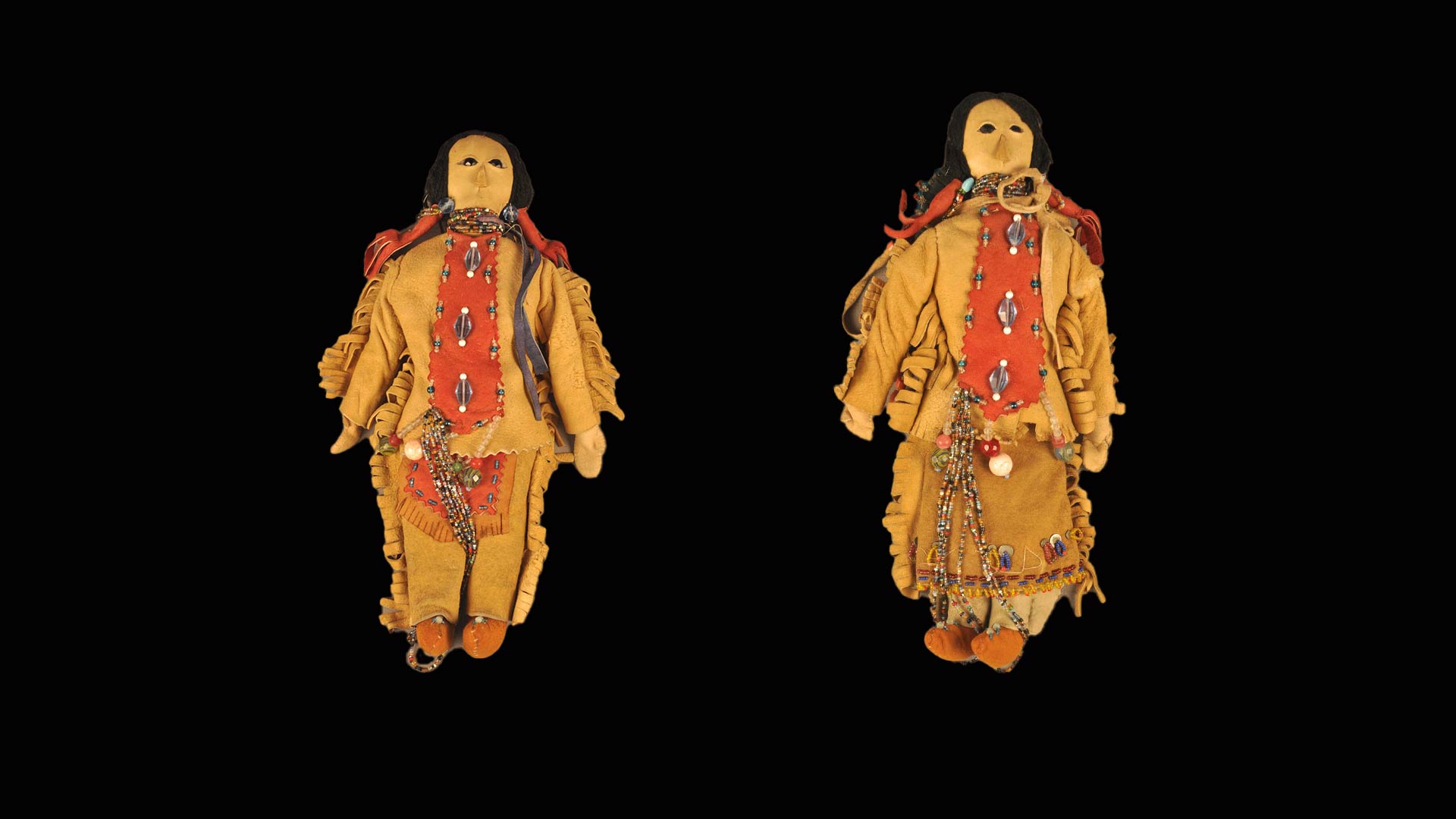 two dolls dressed in leather clothes with a panel in the front of the clothes in a different color and with beadwork throughout