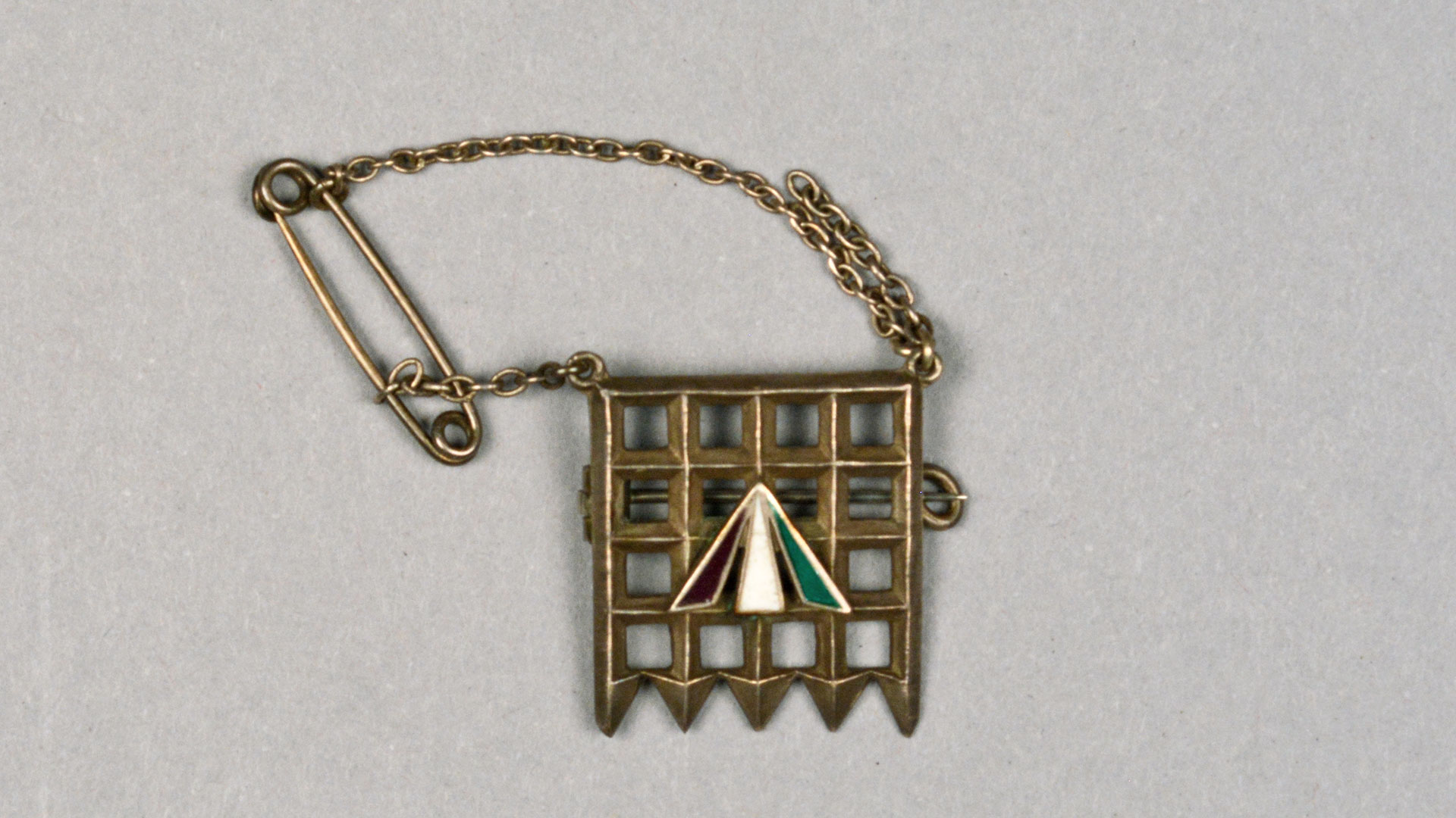 small brass pin with chain, grid design with a three triangle design overlaied in purple, white, and green