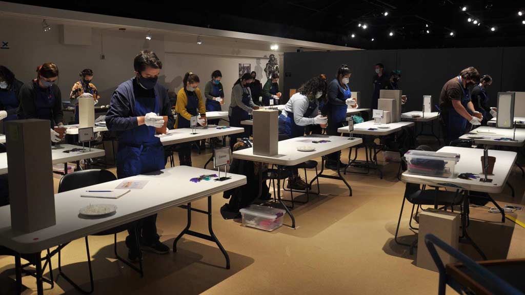 students in masks standing at a table each in the Collaboration and Community Gallery each holding a pot