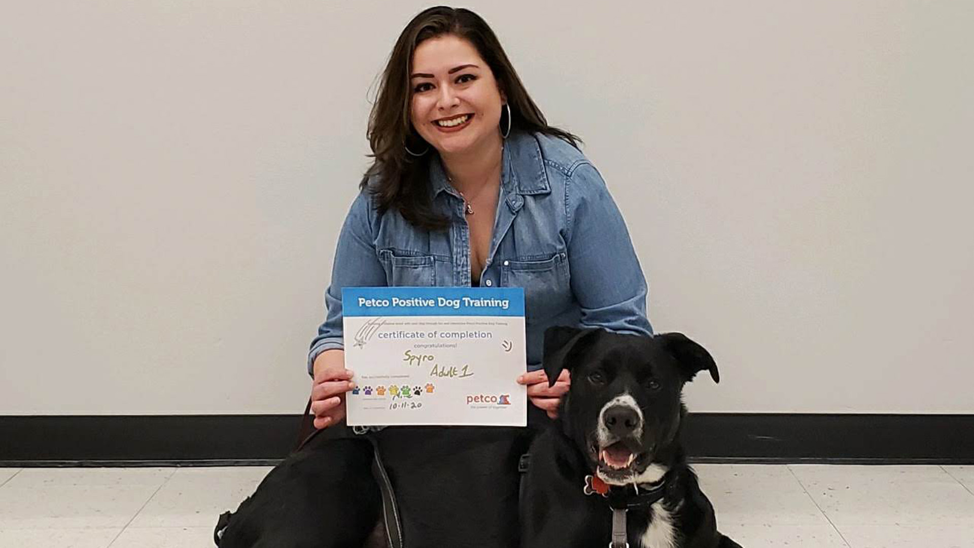 Photo of Allyssa holding a Dog Training certificate of completion next to a black dog.