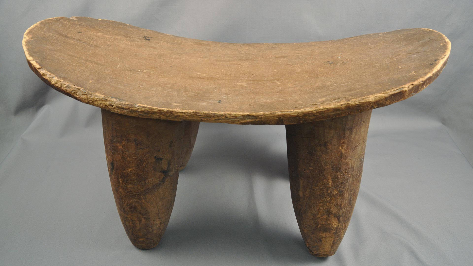 Wooden stool with 4 tapered legs and a slightly curved flat seat