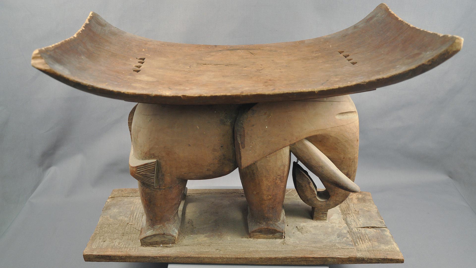 carved elephant with tusks carrying a concave curved seat